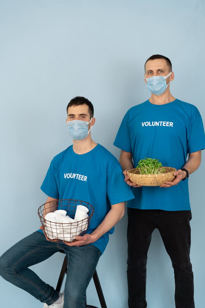 Two volunteers in blue shirts and masks holding eco-friendly supplies indoors.